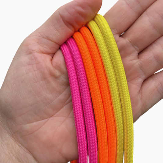 Stylische Handyketten für den Sommer – Neon Pink, Gelb & Orange als Trend-Accessoire.  Eine Hand hält drei leuchtende Handyketten in Neon Pink, Gelb und Orange vor einem hellen Hintergrund.