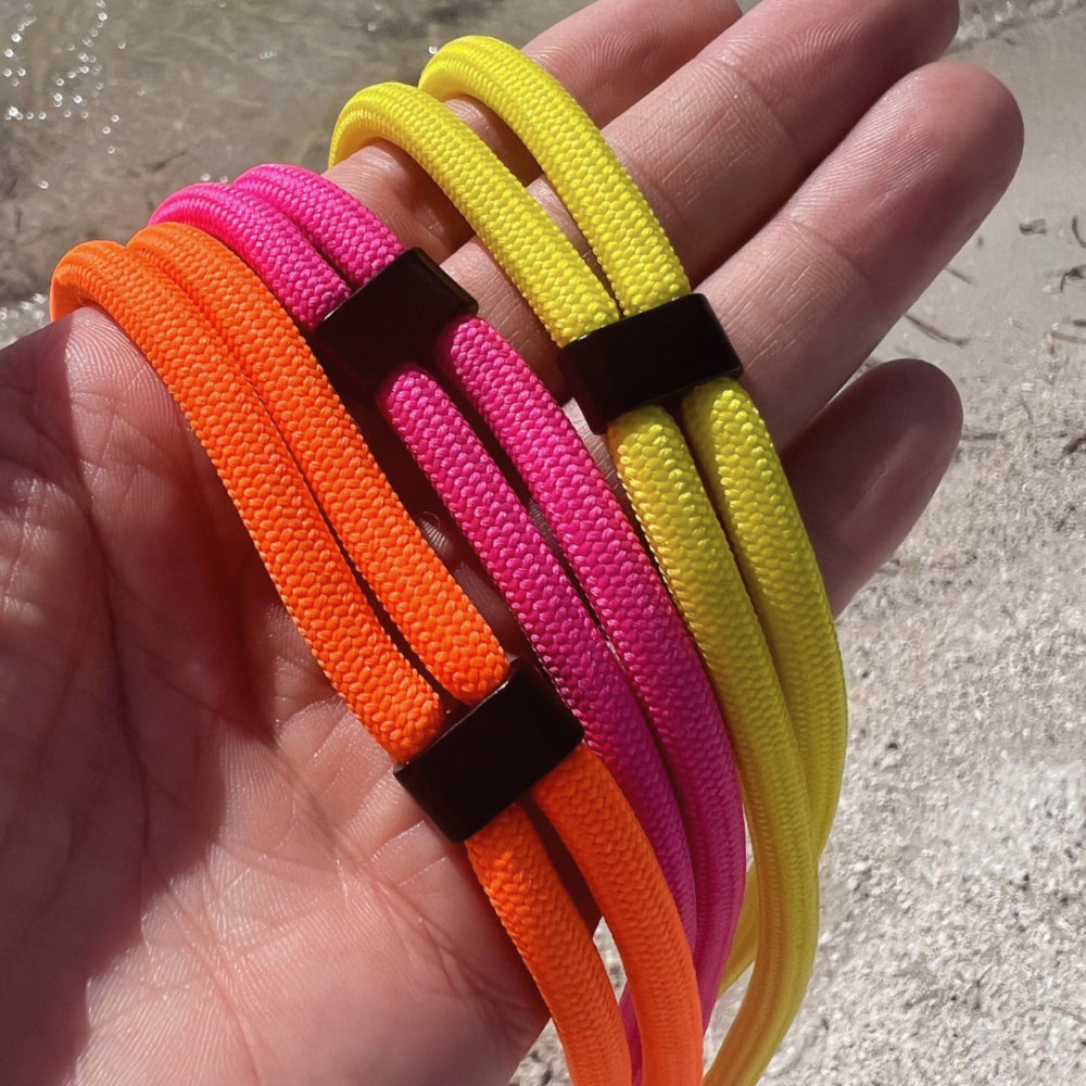 Hand hält bunte Handyketten in leuchtenden Neonfarben – Gelb, Orange und Pink.