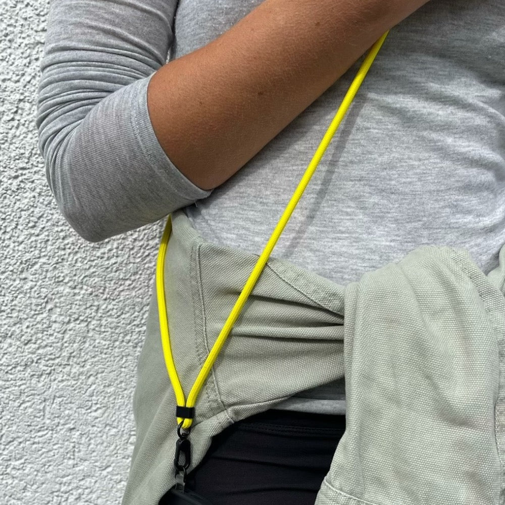 Neon gelbes Handyband im Streetstyle-Look – lässig getragen mit schwarzer Hose und grauem Shirt. Trend-Accessoire: Neon gelbes Handyband für stylische und praktische Handyaufbewahrung.